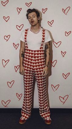 a man with tattoos standing in front of a wall covered in heart shaped paper hearts