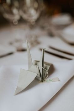 an origami crane is sitting on a table with wine glasses in the background