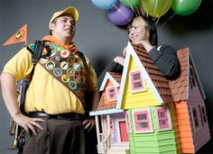 two people standing next to each other in front of a house made out of paper