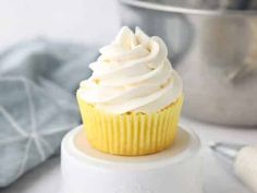 a cupcake with white frosting sitting on top of a cake stand next to a mixer