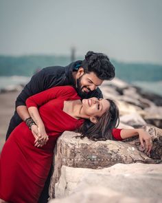 a man and woman embracing each other near the ocean with rocks in the foreground