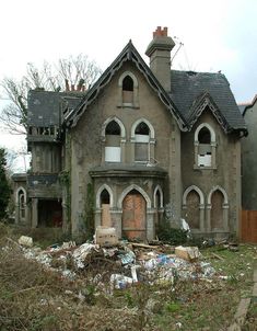 an old abandoned house with lots of windows and debris in the front yard, next to a brick fire hydrant