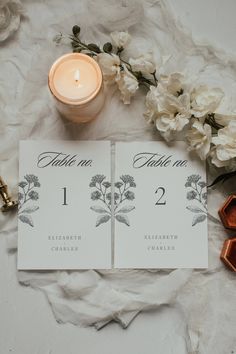 wedding table numbers are displayed next to a candle and some wax cubes on a white cloth