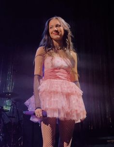 a woman in a pink dress standing on stage with her legs crossed and wearing fishnet stockings