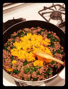 a pan filled with meat and vegetables cooking on top of a stovetop next to a wooden spatula