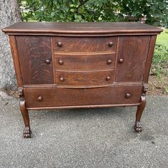 an old wooden dresser sitting in front of a tree on the sidewalk with no one around it