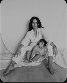 a woman sitting next to a child on top of a white sheeted floor in front of a wall