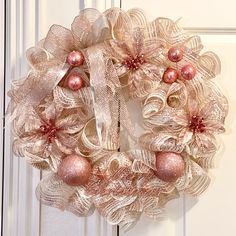 a pink and gold christmas wreath hanging on a door