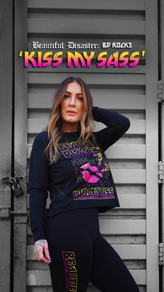 a woman posing in front of a wall with the words kiss my sass on it