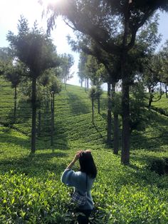 a woman standing in the middle of a lush green field with trees on each side