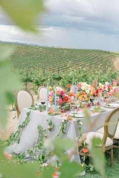 the table is set with flowers and candles for an outdoor dinner in the vineyards