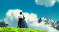 two people standing on top of a lush green hillside under a blue sky with clouds