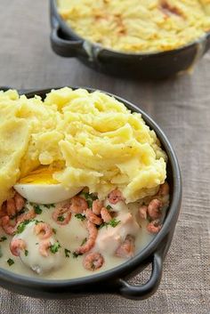 two black pans filled with mashed potatoes, meat and gravy on a table