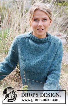 a woman wearing a blue sweater standing in tall grass with her hands on her hips