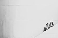 black and white photograph of two people standing at the top of a stair case in front of a wall