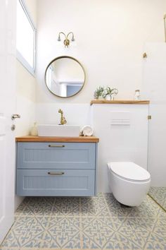 a white toilet sitting next to a blue sink in a bathroom under a round mirror