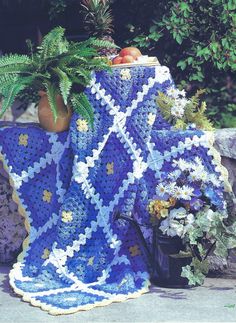 a blue crocheted blanket sitting on top of a table next to a potted plant