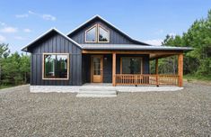 a black house with wood trim on the front porch and covered in gravel, surrounded by trees