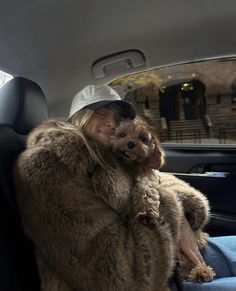 a woman sitting in the back seat of a car holding a dog wearing a hat