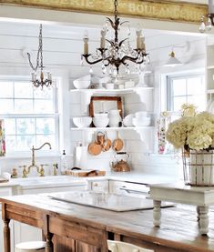 a kitchen with a wooden table and white cabinets, chandelier above the sink