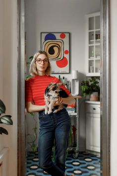 a woman holding a small dog in her arms and looking at the camera while standing in front of a doorway