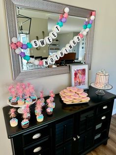 a buffet table with cupcakes, cookies and candy on it in front of a mirror