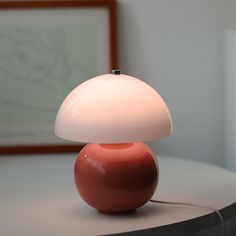 a red lamp sitting on top of a white table next to a framed picture in a room