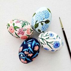 four painted eggs sitting on top of a white surface next to a pencil and paper