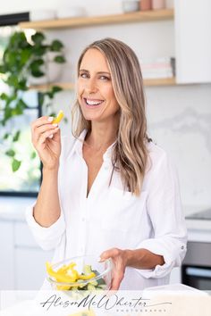 Nutritionist wearing a white shirt standing in her kitchen eating vegetables Nutrition Coach Branding Photos, Nutritionist Photoshoot Ideas, Nutritionist Headshots, Photoshoot In Kitchen, Nutritionist Photoshoot, Kitchen Photoshoot Ideas, Foodie Photoshoot