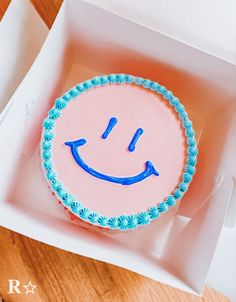 a pink cake with blue icing in a white box on a wooden table top