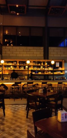 an empty restaurant with tables and chairs in front of the bar, at night time