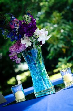 purple and white flowers are in a vase on a blue table cloth with two candles