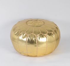 a shiny gold poufce sitting on top of a white surface