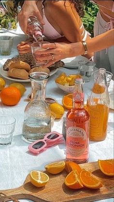 a woman is pouring orange juice into a glass on a table with lemons and cookies