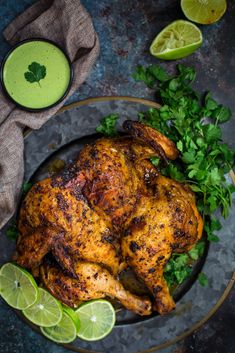 a roasted chicken on a plate with cilantro and limes