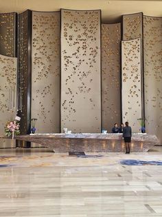 two people sitting at a table in front of some tall wall panels with gold leaves on them