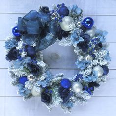 a wreath with blue and silver ornaments hanging on a white wooden wall in front of a house