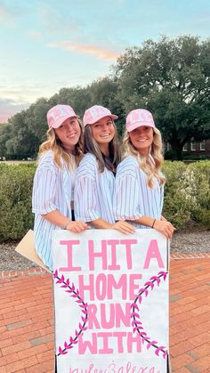 three girls in baseball uniforms are holding a sign