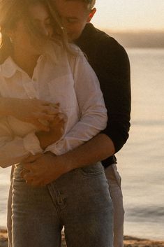 a man and woman hugging on the beach at sunset with water in the back ground