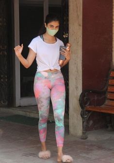 a woman wearing a face mask while standing in front of a building holding a cell phone