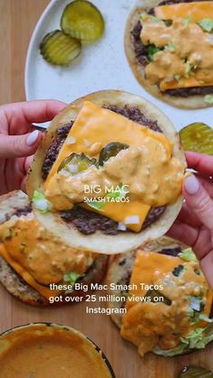 a person holding up a cheeseburger with pickles and sauce on the side