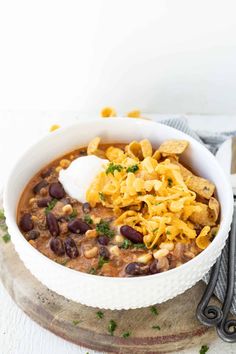 a white bowl filled with chili and beans topped with tortilla chips next to a fork