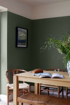 a dining room table with an open book on it and a potted plant in the corner