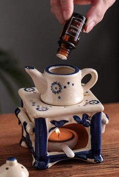 a person is pouring something into a teapot with a candle in it on a table