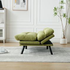 a green couch sitting on top of a rug in a living room next to a potted plant