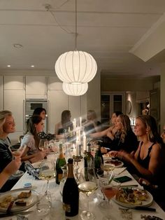 a group of people sitting around a dinner table with food and wine glasses on it