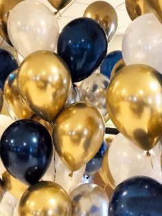 a bunch of balloons that are gold and white with some blue on them in the air