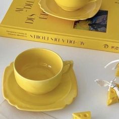 a yellow tea cup and saucer sitting on top of a table next to a book