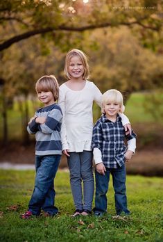 three young children posing for a photo in the grass with their arms around each other