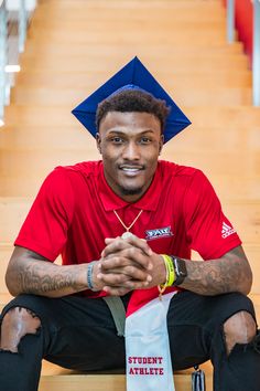 a man in a red shirt is sitting on the stairs wearing a blue graduation cap